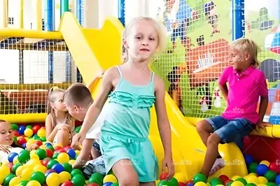 Children playing in colorful ocean ball pit with yellow slide at indoor kids playground