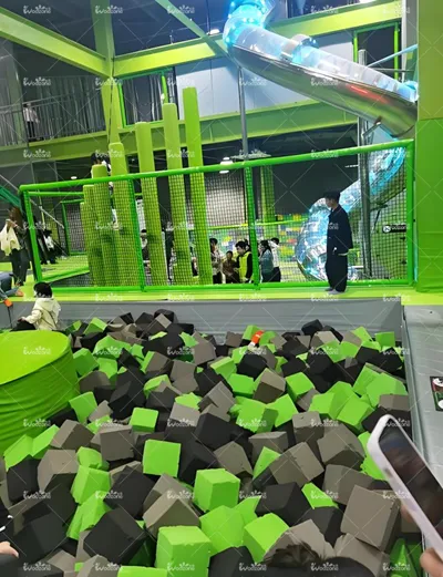 Lime green indoor trampoline park foam pit area equipped with glowing transparent spiral tube slide and full safety netted enclosure