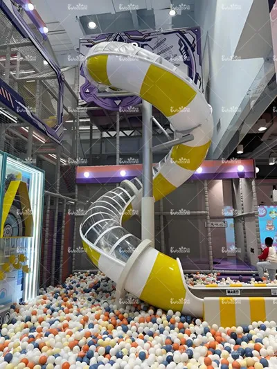 Indoor children's playground featuring a yellow and white spiral slide leading into a large ball pit filled with colorful plastic balls, modern family entertainment center.
