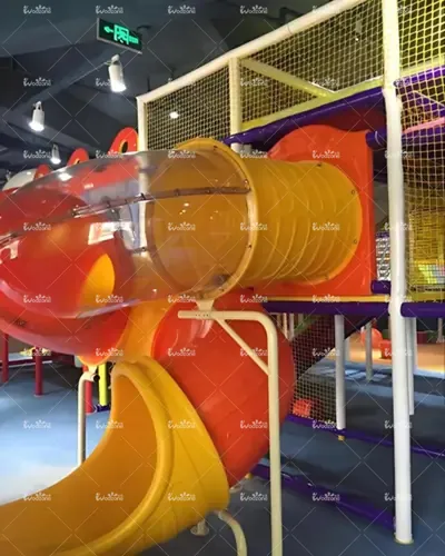 Bright yellow and orange enclosed tube slide in an indoor children's playground, part of a multi-level soft play structure