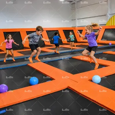 Happy children jumping on interconnected orange and black trampolines in an indoor trampoline park