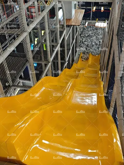 Multi-lane yellow racing slide inside an indoor playground or activity center, featuring a long, steep track for competitive sliding fun.