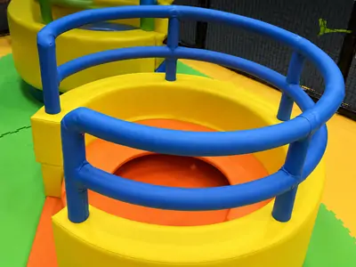 Bright yellow orange soft circular spiral hole kids play equipment with blue padded safety railings inside indoor children playground